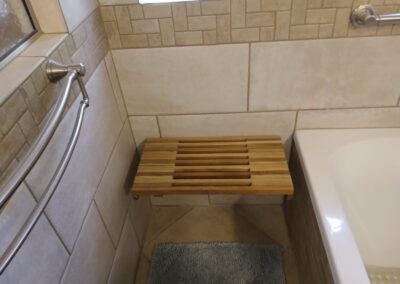 Wooden slatted bath bench mounted to tiled wall beside a bathtub.