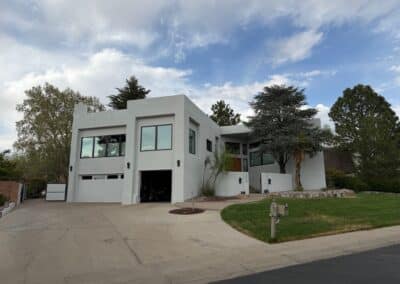 White modern two-story house with large windows, a curved driveway, and surrounding trees under a cloudy sky.